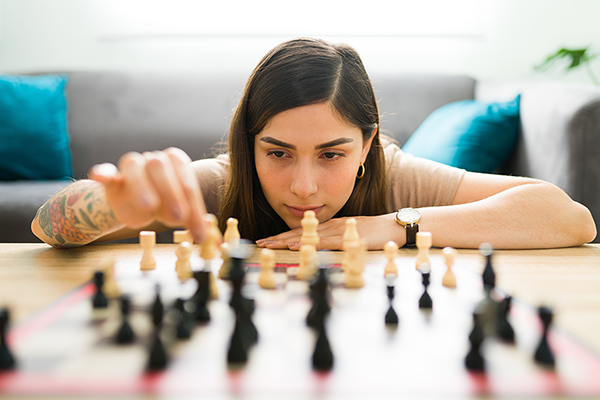 A medium-skinned woman with colorful tattoo on her right arm, moving a white chess piece.