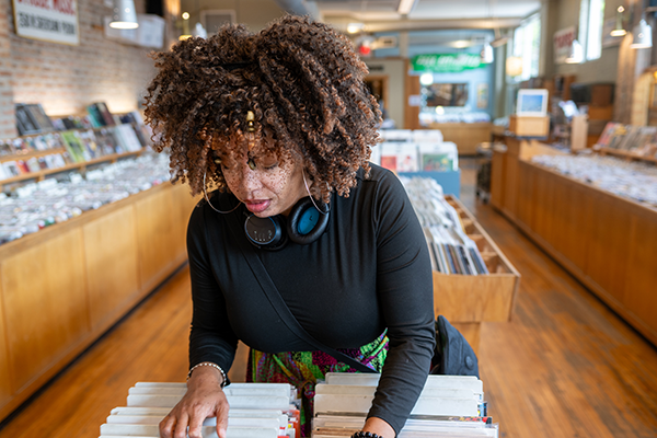 A medium-skinned woman with brown curly hair flipping through vinyl records in a shop.