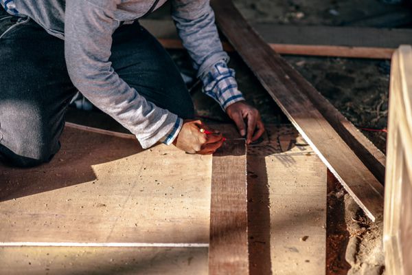 Person kneeling and marking a piece of lumber before cutting it on a construction site. This image is for illustrative purposes only and does not depict individuals in the story.