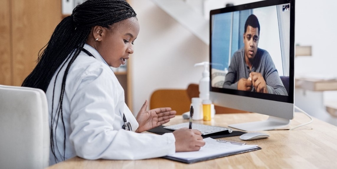 Imagen de una cita de telesalud en el consultorio de un médico. Un médico está hablando con un paciente que está en una pantalla de computadora.