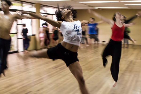 A blurry image of a group of women and men mid-movement, dancing in a dance studio. Photgraph by Michael Zittel.