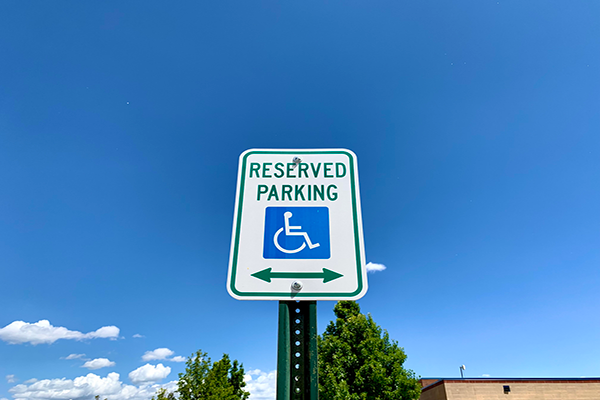 An accessible parking sign with text that reads “reserved parking” with a few green trees and a blue sky.