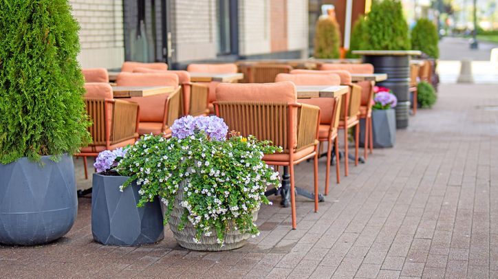 Dining tables and chairs on a deck next to a sidewalk.