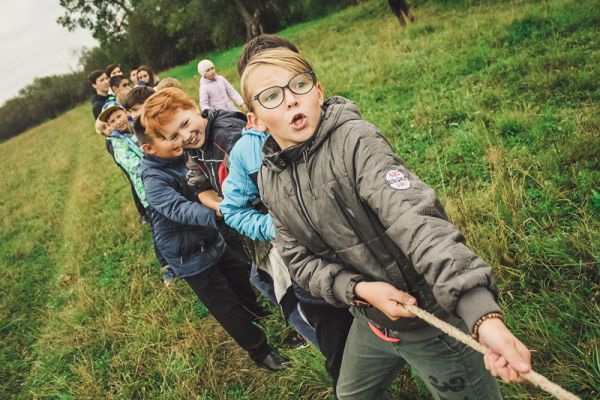 A group of about 12 children playing tug of war in field in the fall. Children are laughing and screaming