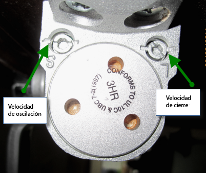 Foto de un cierrapuertas con los tornillos de ajuste etiquetados como "Velocidad de oscilación” y "Velocidad de cierre ".