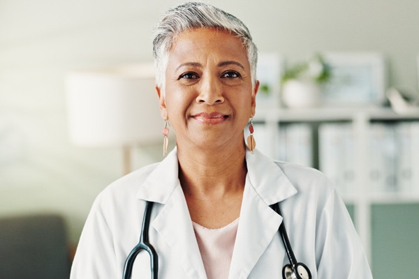 A light-medium-skinned older woman who is a healthcare worker. She wears a white coat and a stethoscope.