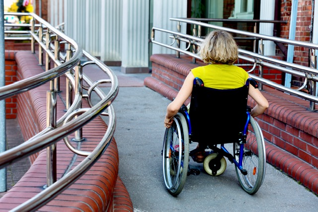 A woman pushing herself in a wheelchair in front of a building